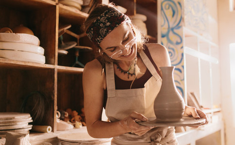 Woman holding a finished clay pot on potters wheel base
