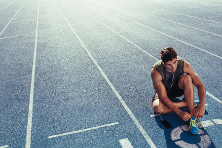 Sprinter tying shoe lace sitting on running track
