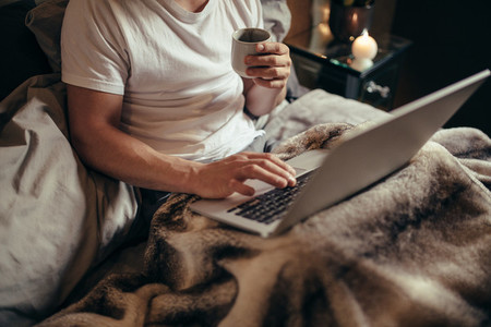 Man on bed using laptop and having coffee