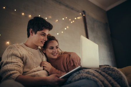 Relaxed couple sitting on sofa using laptop at home