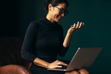 Smiling woman speaking on cellphone and working on laptop