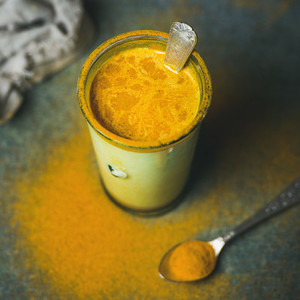 Golden milk with turmeric powder in glass  square crop