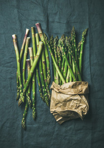 Fresh green asparagus in craft paper bag over grey cloth