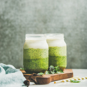 Ombre layered green smoothies with mint leaves in glass jars