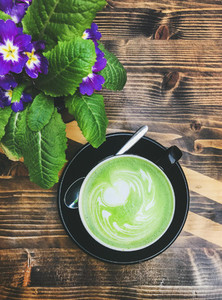 Cup of matcha latte and bright flowers on wooden table