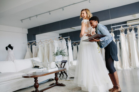 Female trying on wedding gown with women assistant in shop