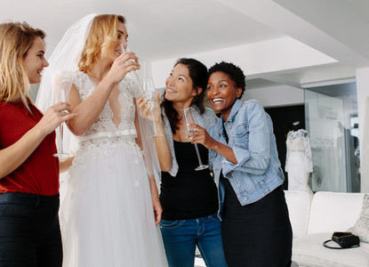 Bride drinking champagne with friends in bridal boutique
