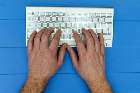 Man typing on wireless computer keyboard on blue wood desk