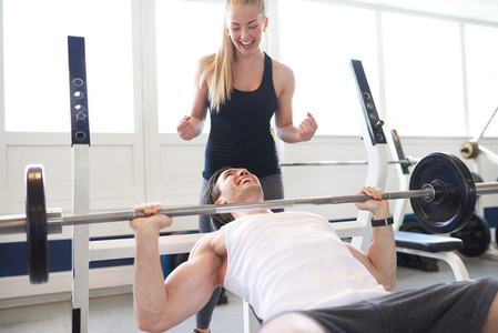Woman Spotting Man Lifting Barbell in Gym