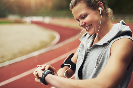 Fit young woman looking at her watch while standing on track field