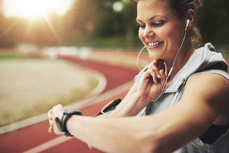 Smiling athletic woman looking at her watch and feeling the pulse on track field