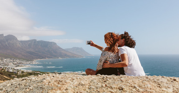 Couple sitting on the top of mountain and taking selfie