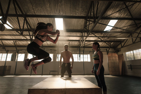 Woman jumping on wooden box guided by trainer