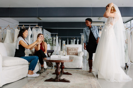 Woman trying on wedding dress in a shop with friends