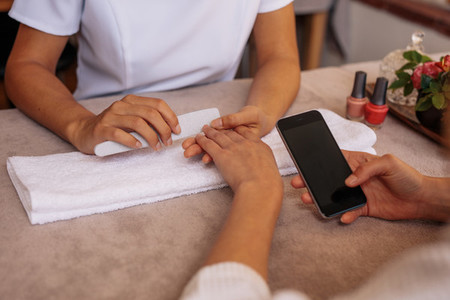 Female with smartphone getting manicure at spa