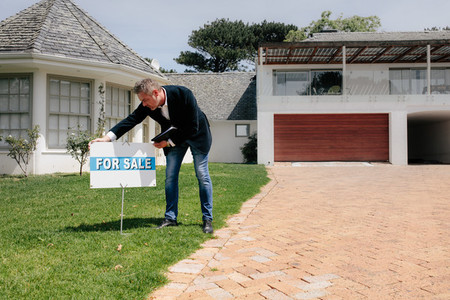 Real estate agent with for sale sign outside a new house