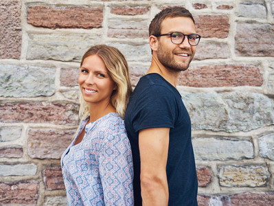 Smiling Couple Standing Back to Back Against Wall