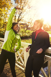 Two smiling sportswomen stretching on bridge