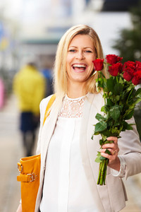 Professional white woman posing on sidewalk holding red roses