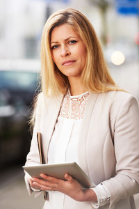 Professional woman posing on sidewalk with tablet
