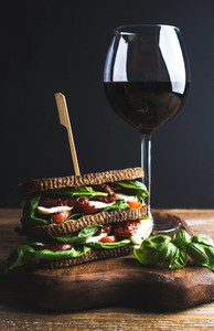 Homemade caprese sandwich and glass of red wine on board