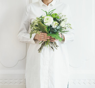Young woman wearing white clothes holding bouquet  white wall background