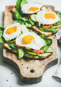 Bread toasts with fried eggs and fresh vegetables on board