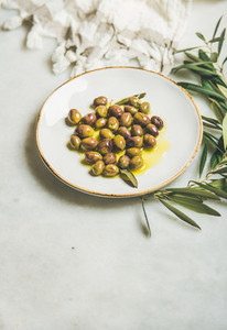 Pickled green Mediterranean olives in olive oil on white plate