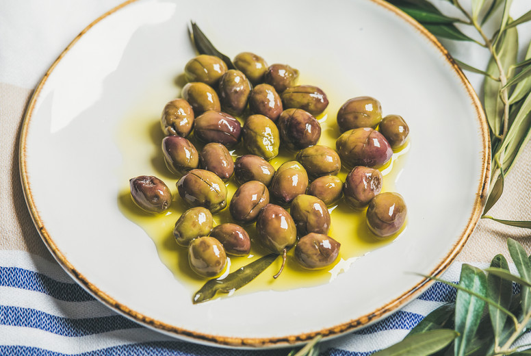 Pickled green Mediterranean olives and olive tree branch on towel