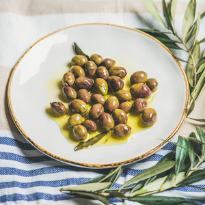Pickled green Mediterranean olives and olive tree branch on towel