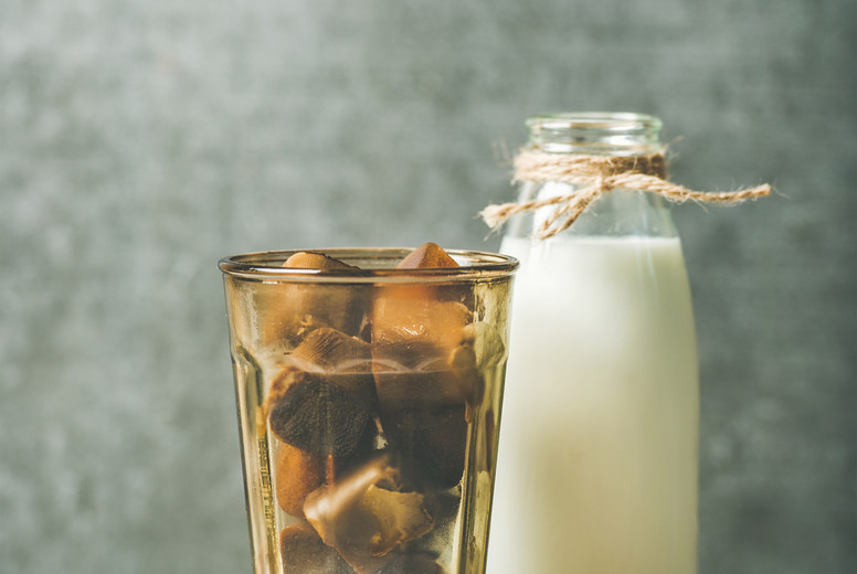 Glass with frozen coffee ice cubes and milk in bottle