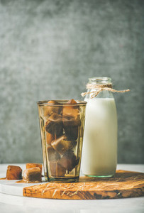 Glass with frozen coffee ice cubes and milk in bottle