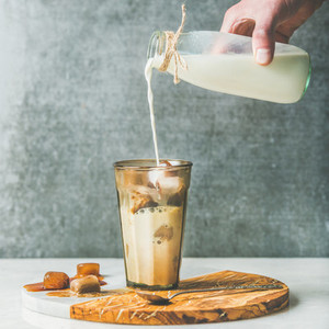 Mans hand pouring milk to Iced latte summer coffee cocktail