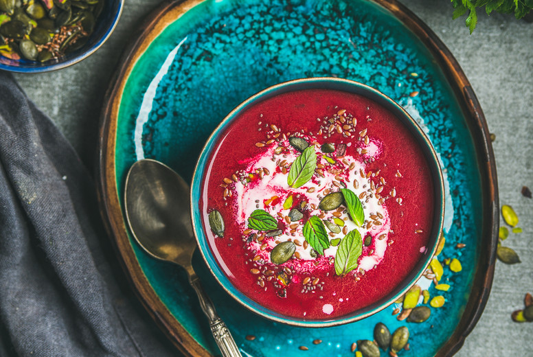 Spring beetroot soup on bright blue plate over gery background