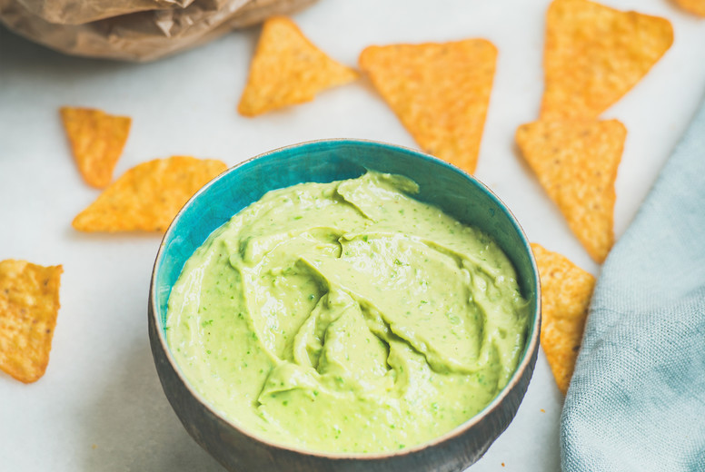 Mexican corn chips and fresh guacamole sauce over marble background