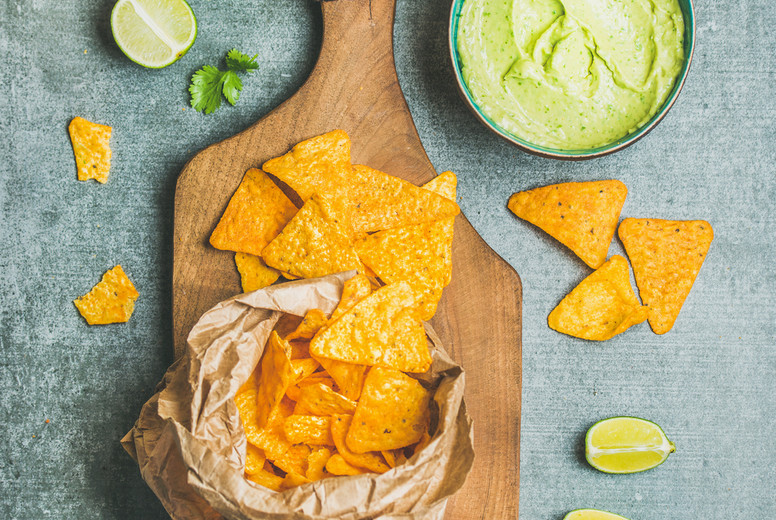 Mexican corn chips and fresh guacamole sauce on wooden board