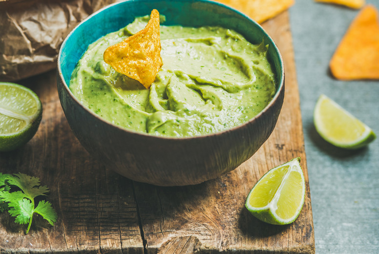 Fresh guacamole sauce in blue bowl and chips, square crop