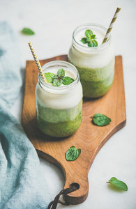 Ombre layered green smoothies in glass jars with straws