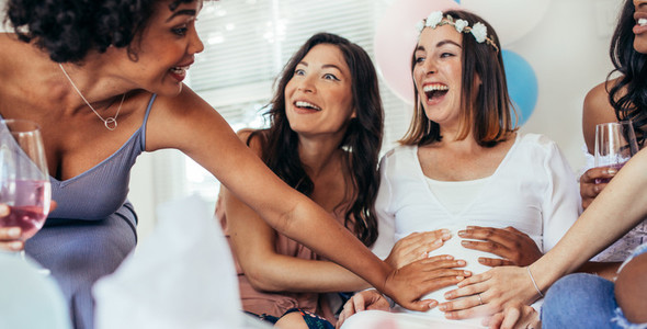 Friends touching pregnant womans belly at baby shower party
