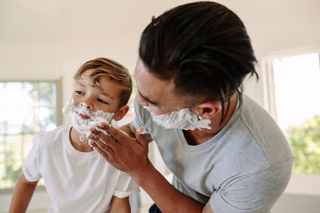 Man applying shaving foam in his sons face