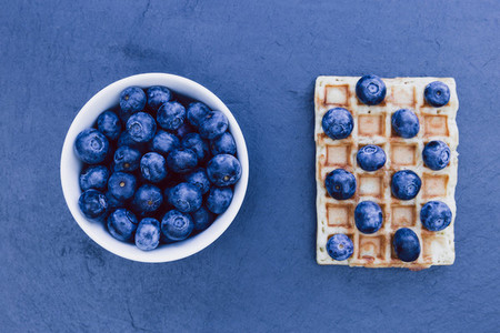Waffles and white bowl of blueberries for breakfast on dark back