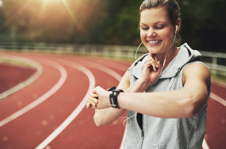 Athletic young woman looking at her watch while listening to music