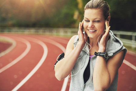 Smiling woman listening to music on track field