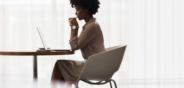 Businesswoman drinking coffee and looking at laptop