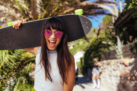Smiling woman walking outdoors holding skateboard