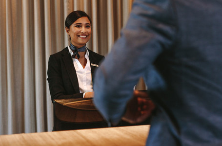 Smiling hotel receptionist attending guest at check in counter