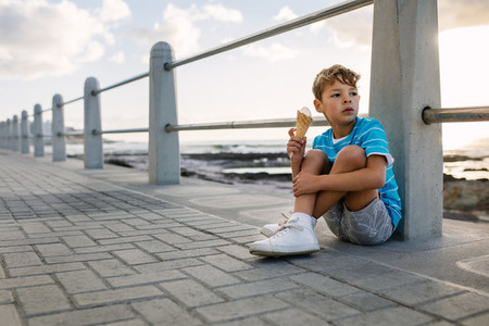 Boy eating an ice cream sitting near seafront