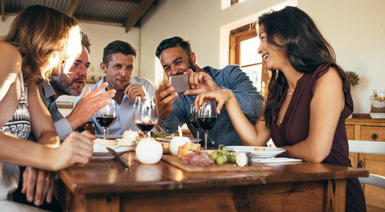 Friends at dinner party looking pictures on smartphone