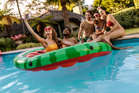 Joyful friends with drinks taking selfie by the pool