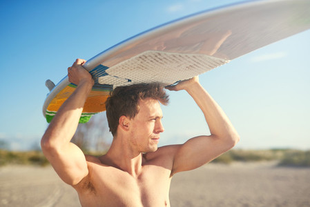 Handsome strong surfer carrying his surfboard